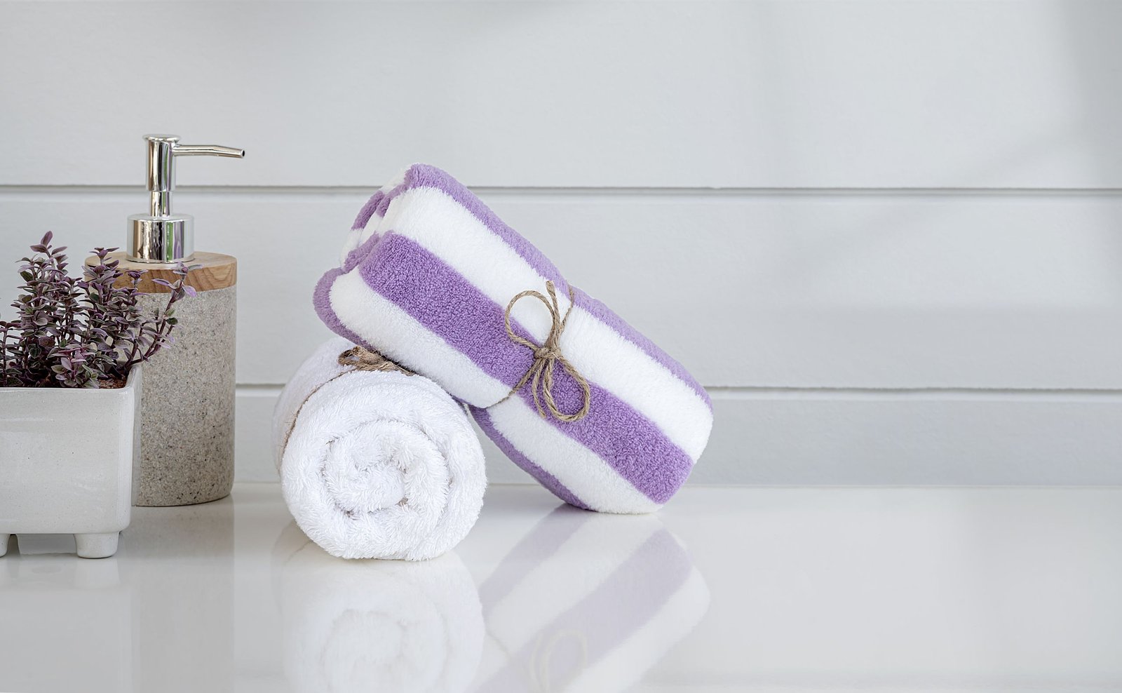 Roll of white spa towel tied with hemp rope on white counter table, copy space.